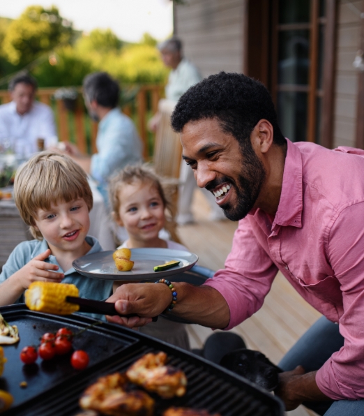 A man cooks on a grill with two children looking on.